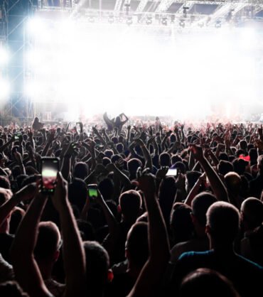 Back view of excited audience with arms raised cheering in front of the stage at music concert. Copy space.