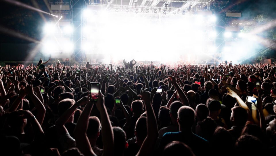 Back view of excited audience with arms raised cheering in front of the stage at music concert. Copy space.